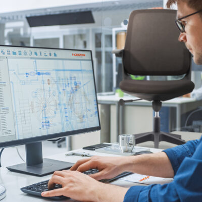 Over the Shoulder Shot of Engineer Working with CAD Software on Desktop Computer, Screen Shows Technical Drafts and Drawings. In the Background Engineering Facility Specialising on Industrial Design Over the Shoulder Shot of Engineer Working with CAD Software on Desktop Computer, Screen Shows Technical Drafts and Drawings. In the Background Engineering Facility Specialising on Industrial Design